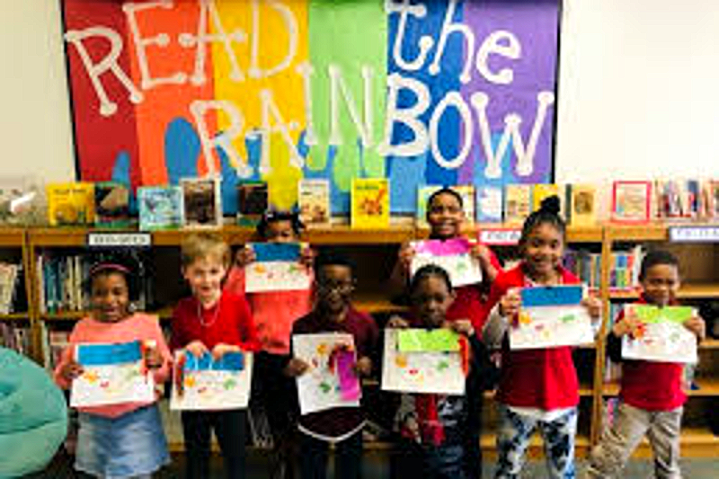Beacon students holding up their work in front of the Read the Rainbow library display